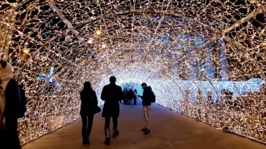 Cenova, İtalya - 11 / 19 / 2019: Kırmızı beyaz ve turuncu renkli kurşun ışık galerisi. Düşük açı. İnsanlar Noel süslemelerinin tadını çıkarıyor..