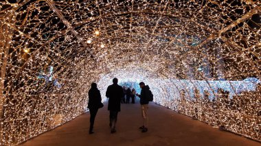 Cenova, İtalya - 11 / 19 / 2019: Kırmızı beyaz ve turuncu renkli kurşun ışık galerisi. Düşük açı. İnsanlar Noel süslemelerinin tadını çıkarıyor..