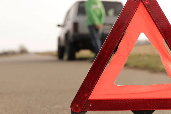 Red triangle of a stopped car on the road. An emergency stop sign mounted on the road against the background of stopped car. The concept of safe traffic on the road.