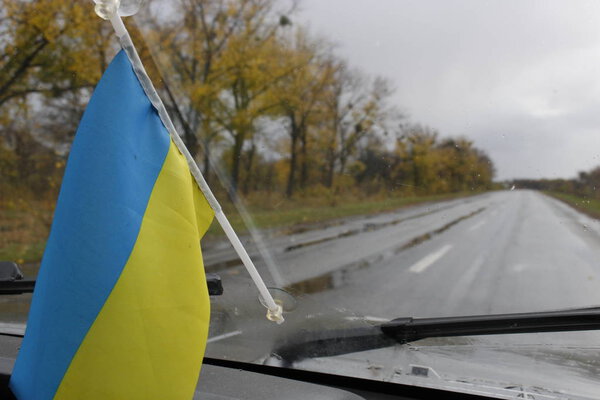 The Ukrainian flag is mounted on the windshield of the car. It's rain, autumn.