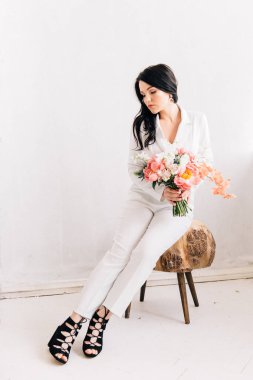 Beyaz pantolon giymiş şık bir gelin ve canlı mercanların şık tonlarında bir buket.