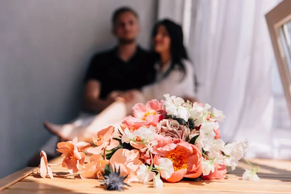 wedding bouquet and grooms boutonniere in trend color according to panton live coral with a couple in the background