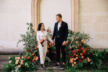 Gelin ve damat alışılmadık bir mercan rengi çiçek kompozisyonu üzerine poz veriyorlar. Düğün merasimi için.