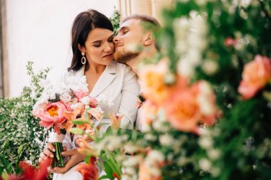 Gelin ve damat çiçek desenleri arasında nazikçe poz veriyor. Renkli mercan renginde. Açık hava düğün töreni için yaratılmış.