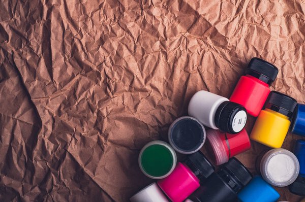 top view of colorful oil paint bottles for textile on crumpled kraft paper surface