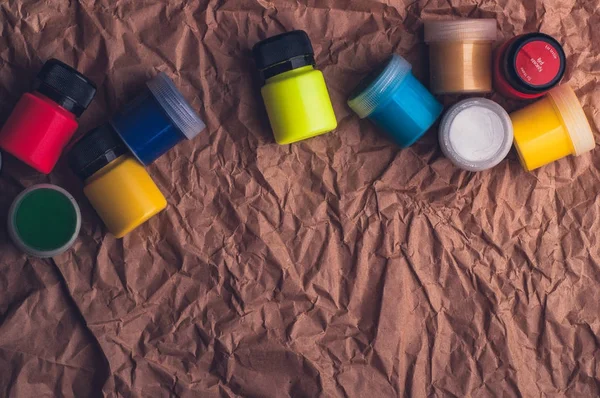 top view of colorful textile paint bottles on crumpled kraft paper surface