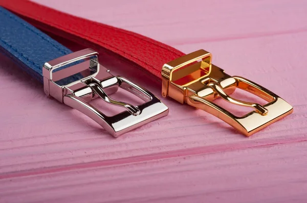 two belts with buckles on pink surface