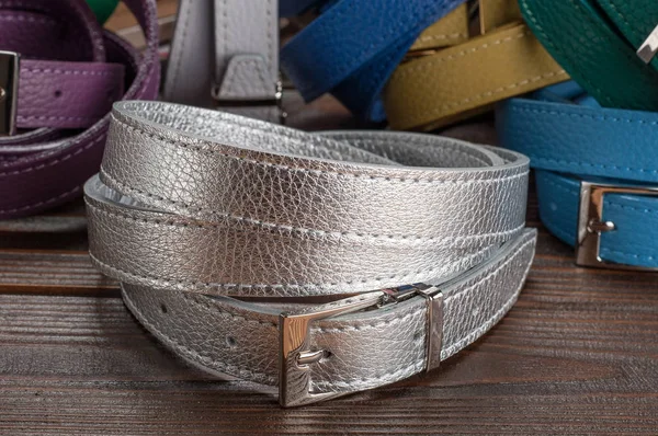 female silver colored belt on wooden surface with trouser belts on background