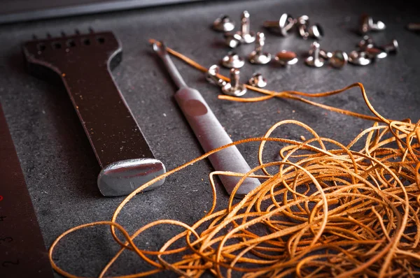 brown leather ropes, metal buttons and prong chisel on gray surface table
