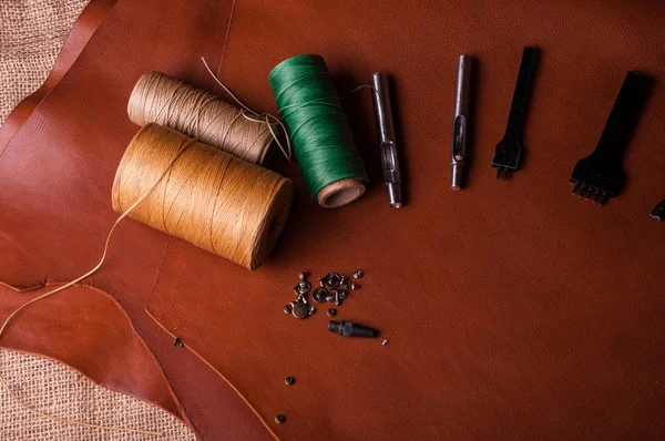 tailor tools and threads on brown leather surface in workshop