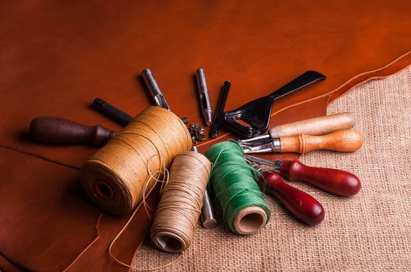 leather fabric and burlap surface, sewing spools of threads and leather craft tools