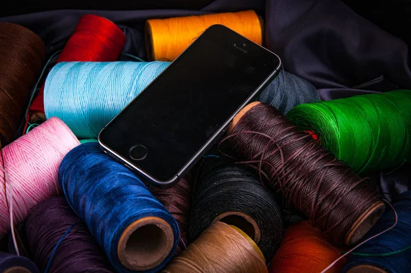 colorful bobbins of threads and mobile phone
