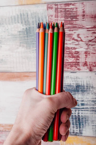 human hand holding multicolored pencils