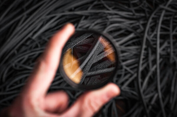 male hand holding magnifying glass above black leather ropes