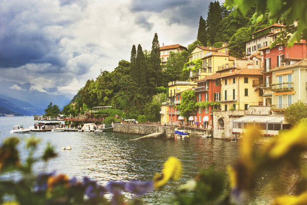 Beautiful cityscape with a Como lake coastline of italian Varenna city with colorful building, big trees, and dramatic sky before the rain