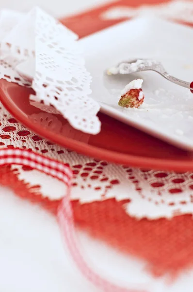 Remains of baba with a cream and strawberries in white and red plates — Stock Photo, Image