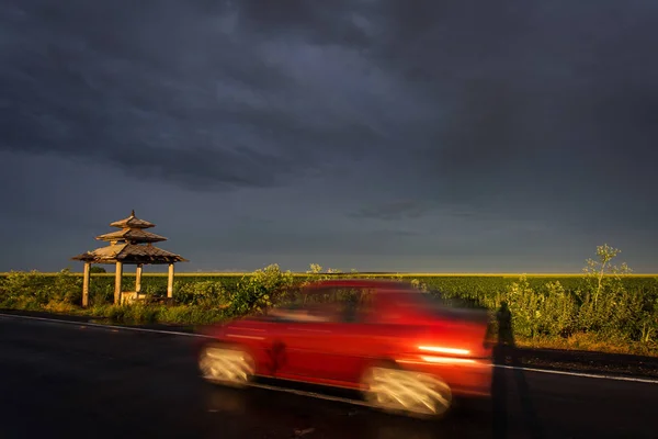 Auto rossa in movimento su strada con nuvole tempesta in background — Foto Stock