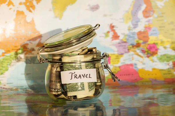 Oszczędność pieniędzy podróży w szklanym słoju z mapy w tle — Zdjęcie stockowe