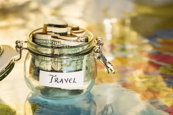 Viajar poupança de dinheiro em um frasco de vidro com mapa no fundo — Fotografia de Stock