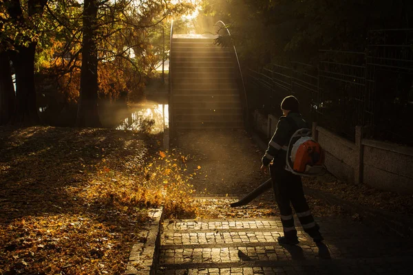 Homem limpando o parque de folhas na temporada de outono ao nascer do sol — Fotografia de Stock