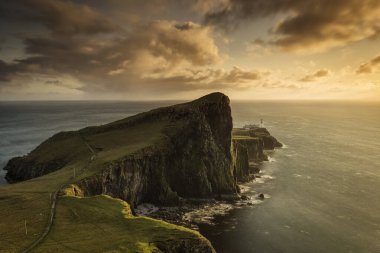 Neist Point ve Skye Adası 'ndaki deniz feneri gün batımında arka planda güzel renkli bulutlarla İskoçya, U