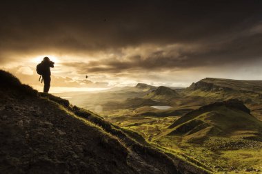 İskoçya 'nın dağlık bölgelerinden Skye Adası' ndaki Quiraing dağlarının manzaralı çekimini yapan fotoğrafçı silueti. Renkli bir Rayini bulutu ile gün doğumu zamanı