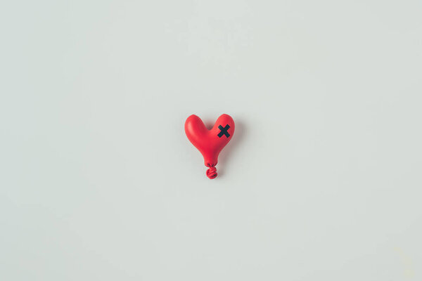 top view of deflated heart shaped balloon with insulating tape cross isolated on white, valentines day concept