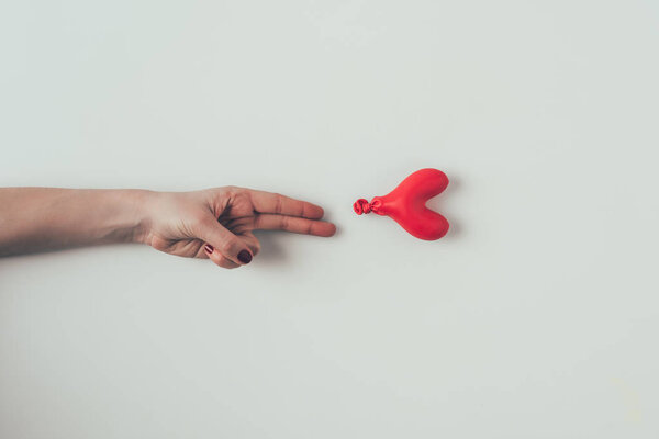 cropped image of woman reaching out deflated balloon with two fingers on white, valentines day concept