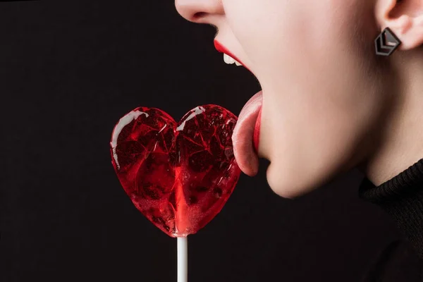 裁剪图像的女人舔心形棒棒糖孤立在黑色 情人节日的概念 — 图库照片