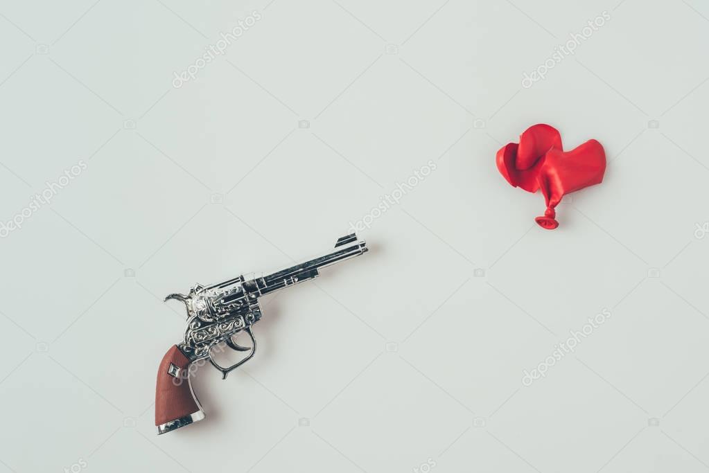 Top view of gun barrel aiming at broken heart shaped balloon isolated on white, valentines day concept
