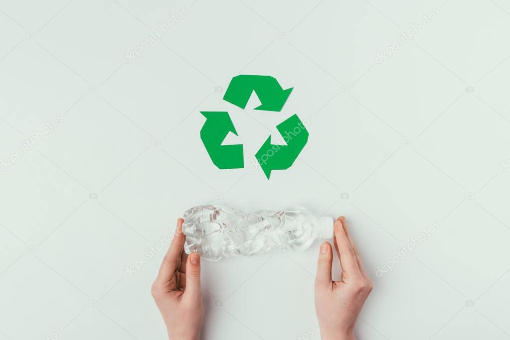 partial view of woman holding plastic bottle with recycle sign isolated on grey