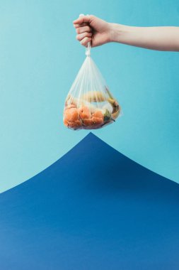 cropped shot of woman holding plastic bag with trash on blue background clipart