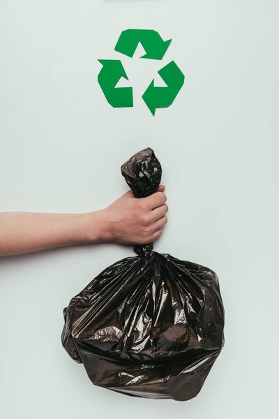 cropped shot of woman holding garbage bag in hand with recycle sign isolated on grey