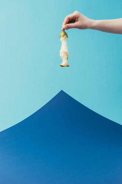 частичный вид женщины, держащей грушевое ядро в руке на синем фоне
