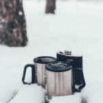 Close up view of thermocups and flask in snow on winter day in forest