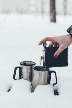 partial view of woman pouring coffee into cups in snow in winter