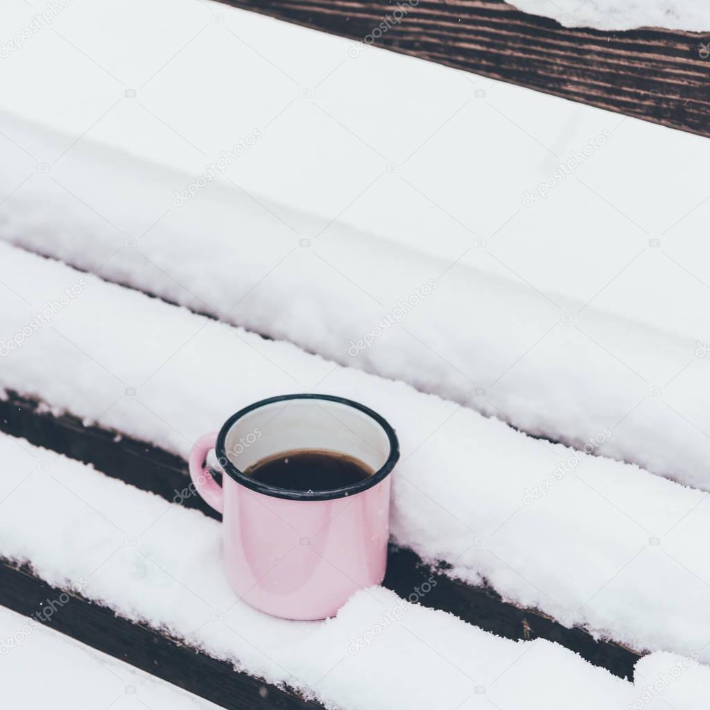 close up view of cup of coffee on wooden bench on snowy day