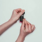 Partial view of woman opening condom isolated on grey