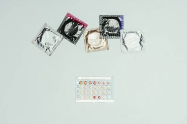 top view of arranged condoms and contraceptive pills isolated on grey clipart