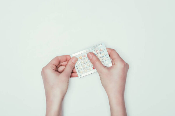 cropped shot of woman holding contraceptive pills in hands isolated on grey