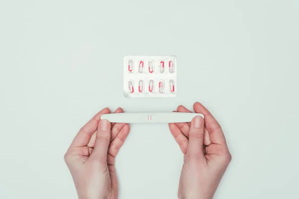 手とグレーに分離された経口避妊薬の妊娠テストを保持している女性の部分的なビュー — ストック写真