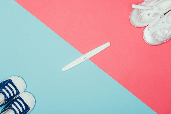 top view of arrangement of  childish shoes and pregnancy test