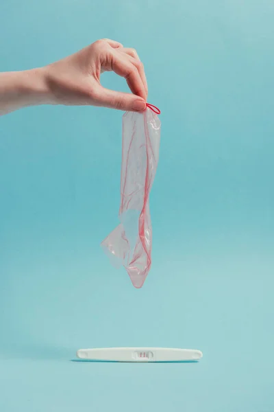 コンドームを手にリッピングを持った女性のショットをトリミングし 青に分離された妊娠検査 — ストック写真