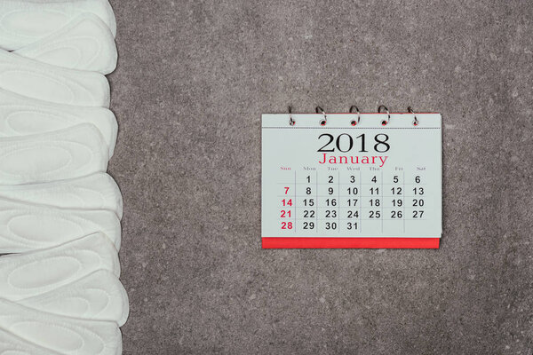 top view of arranged menstrual pads and calendar on grey surface