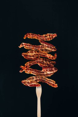 close up view of pieces of bacon on fork isolated on black