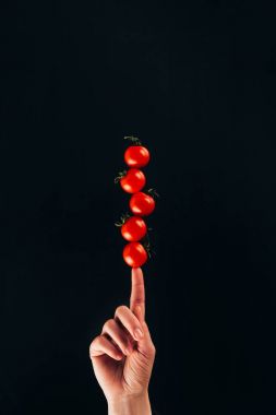 cropped shot of woman holding cherry tomatoes on finger isolated on black clipart
