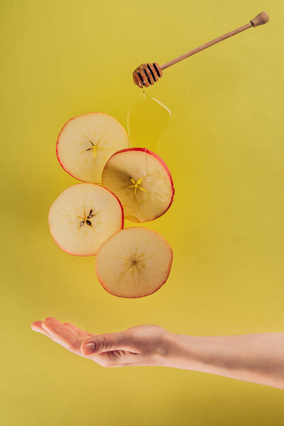 partial view of female hand and levitating pieces of apple with honey