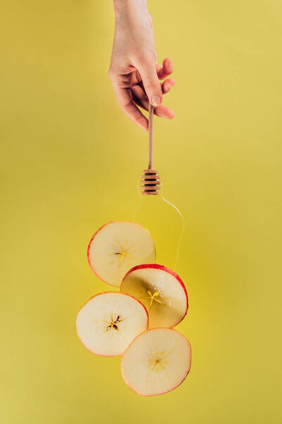 partial view of female hand and levitating pieces of apple with honey