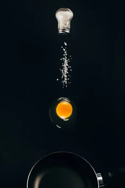 黑煎锅上生蛋黄和盐落的近观 — 图库照片