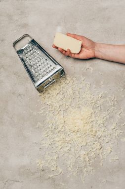 Close-up view of hand holding cheese by grater on light background clipart